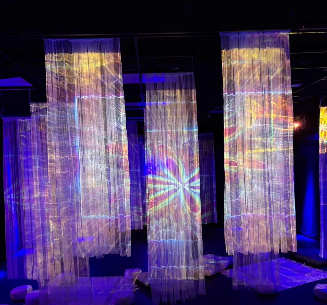 Des rideaux de voile éclairés par le mapping, avec des poufs au sol, dans la salle